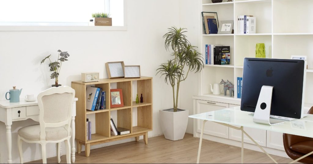 Bright home office featuring cube shelves with books, a small desk and vintage white chair under the window, and a modern desk with a large monitor